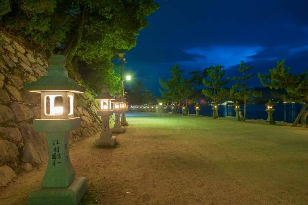 Miyajima Island at Night. Stone lanterns running along the street to the left, and the ocean to the right.