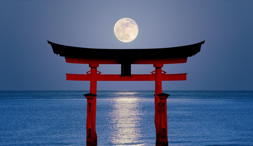 Miyajima Toori Gate at Night with a full moon in the sky in the background.