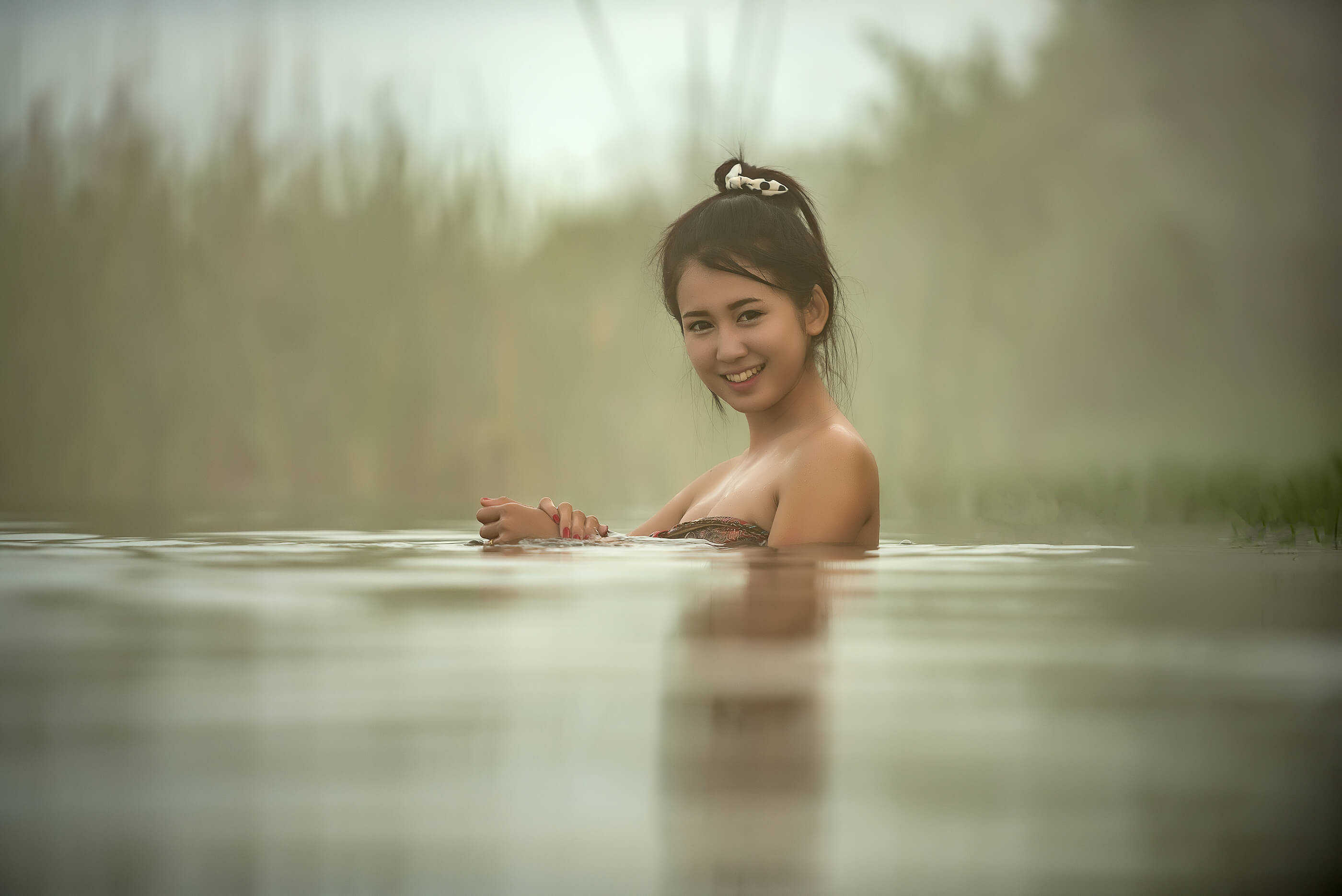 A young Asian woman in an outdoor hot spring. She is looking and smiling at the camera.