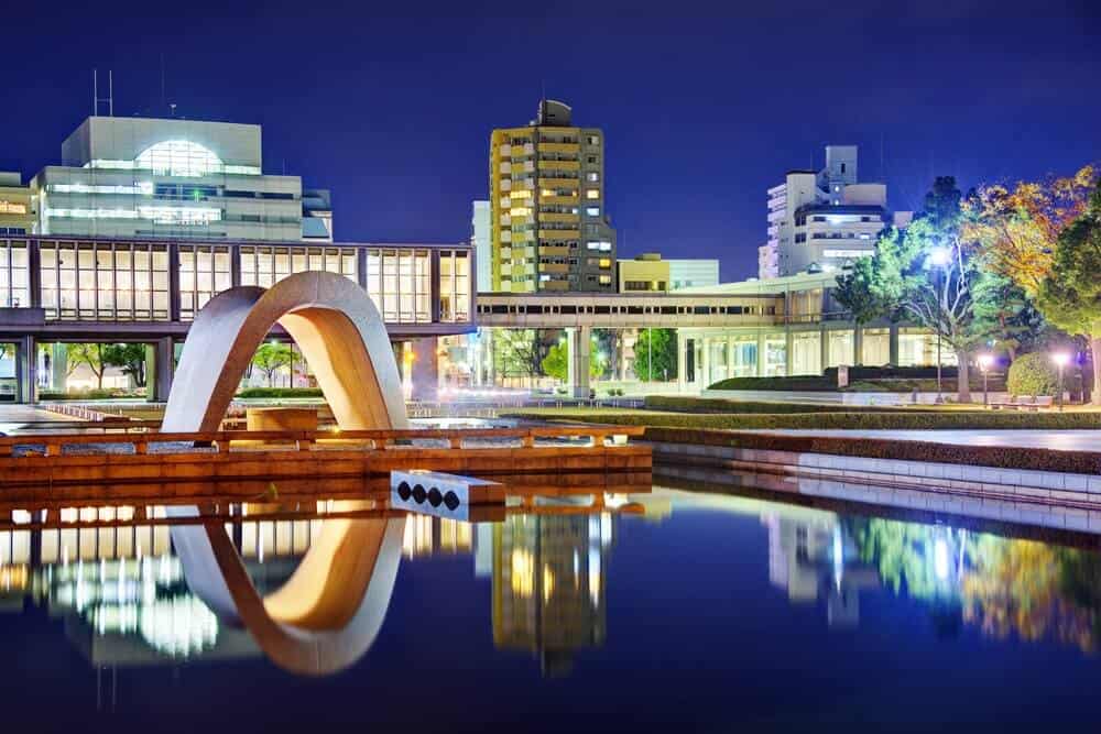 A area around the Hiroshima Peace Memorial Museum at night, with the building reflecting off of the water in the pond.