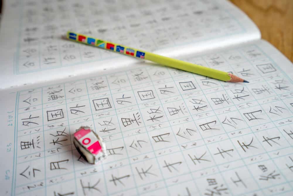 A book filled with handwritten kanji characters with a yellow pencil and eraser on top of it.