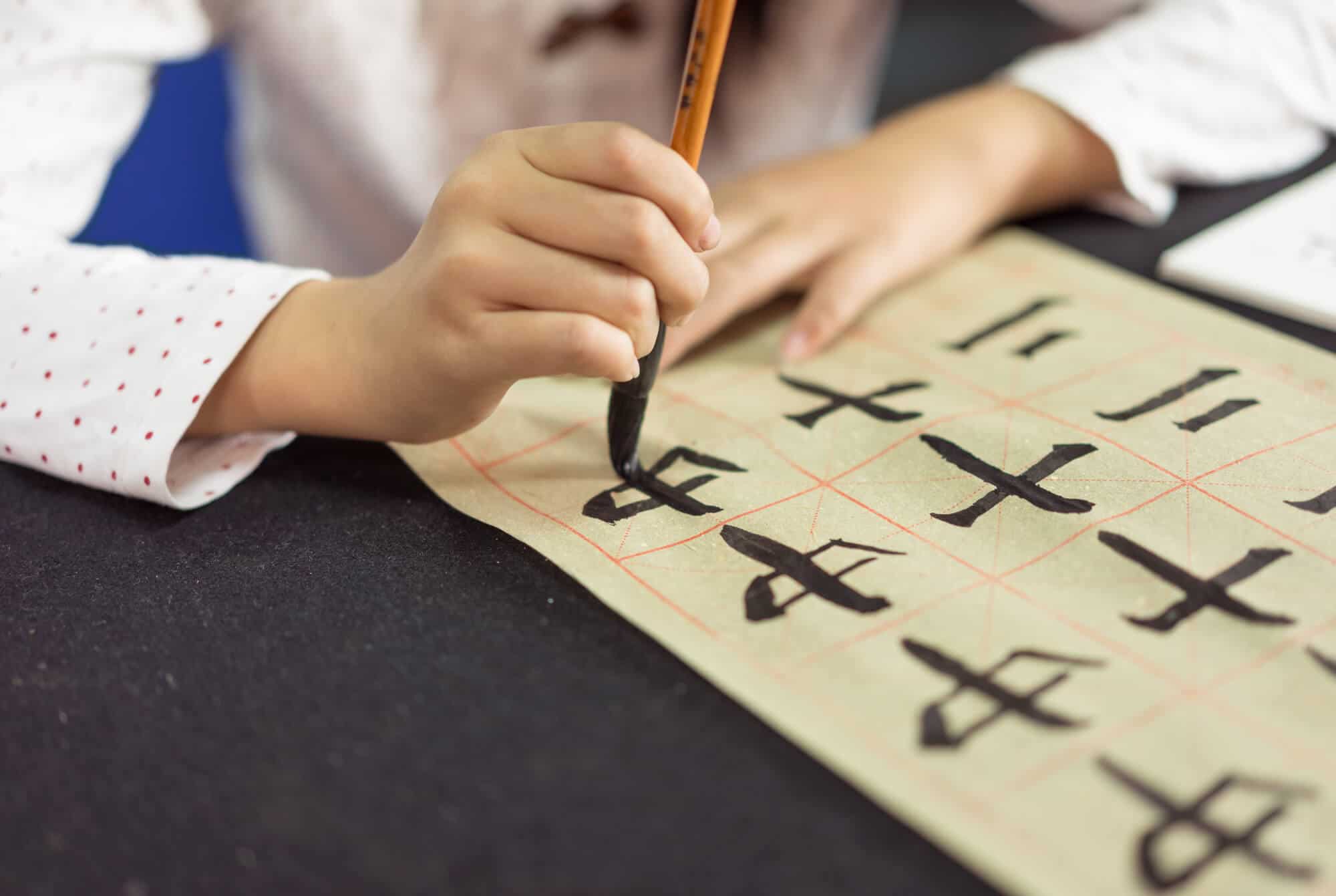 Chinese children learn to write Chinese characters, calligraphy is the traditional culture of China. Someone is writing some characters with a black brush on a piece of paper.