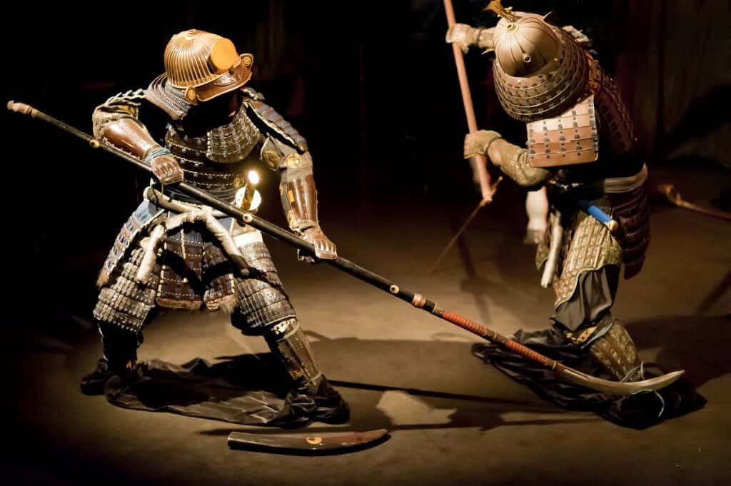 Two old fashioned looking samurai warrior figures in a fighting pose with weapons fighting each other.