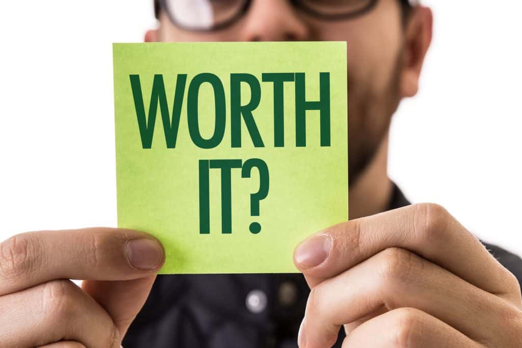 Man holding up a green Post It sized paper that says "WORTH IT?"