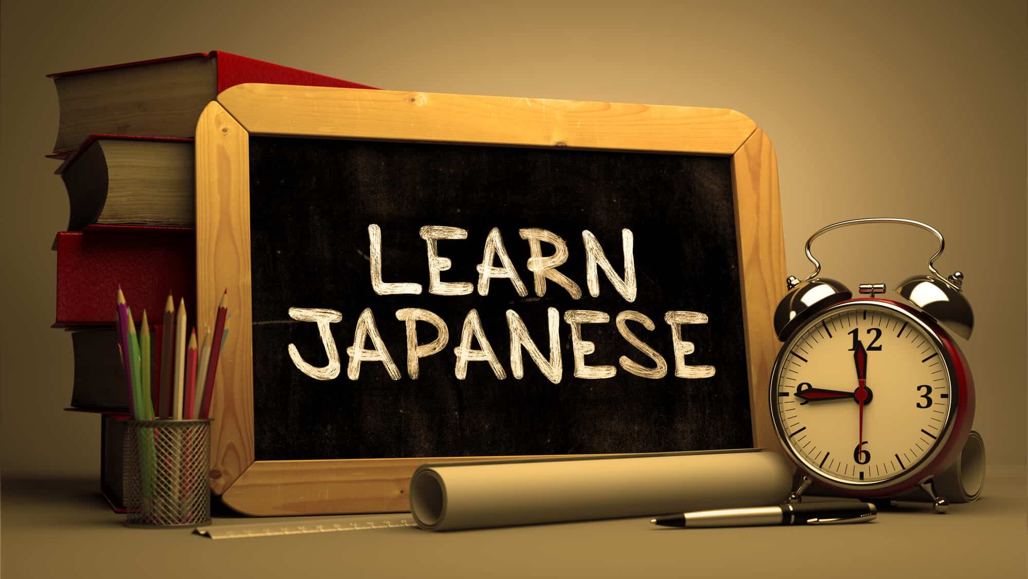 A small rectangular chalkboard with the words, "LEARN JAPAENSE" written on it in white chalk. Behind the chalkboard are a stack of books. In front of it is an alarm clock, paper rolled into a tube. a pen, and a ruler. On the right side is a pencil holder with pencils in it.