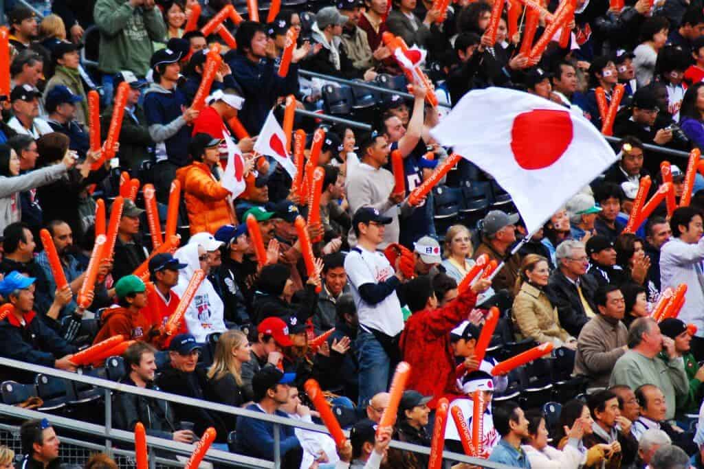 A group of Tokyo Baseball Japanese Fans cheering in the stands awith one group holding a flag of Japan.
