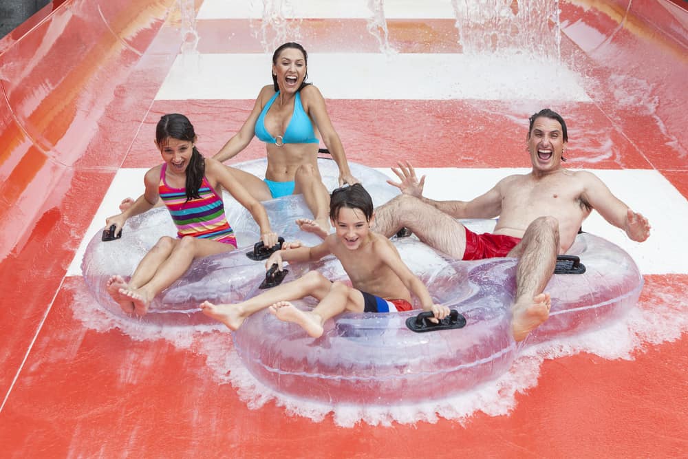 A man, woman, boy, and girl are sliding down a waterslide on clean inner tubes.