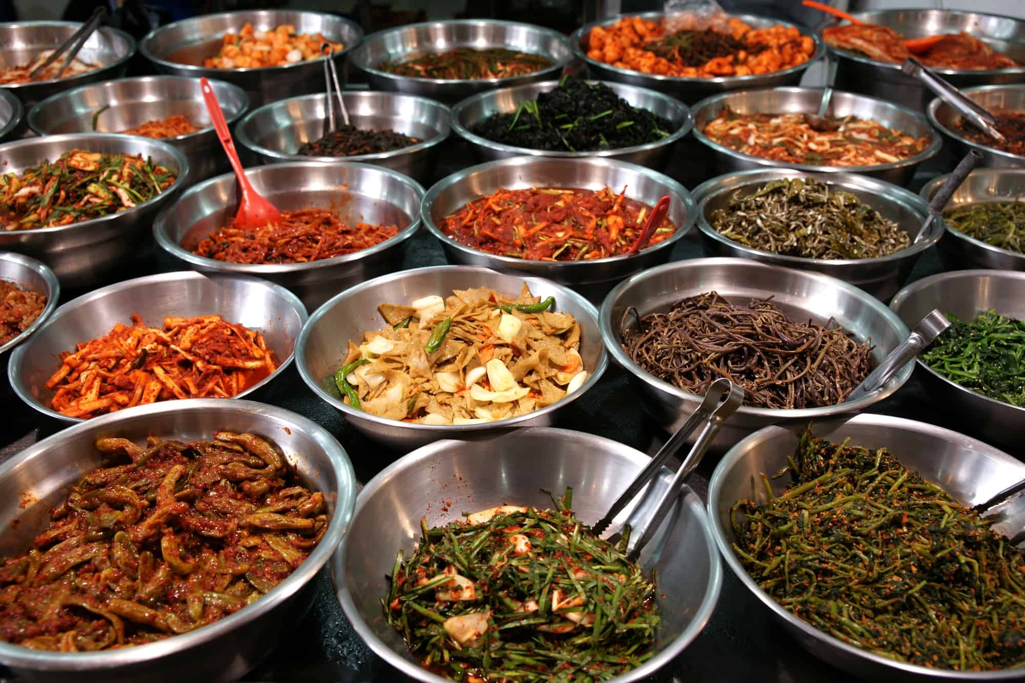 Silver metal bowls filled with various Korean dishes (mostly vegetables).
