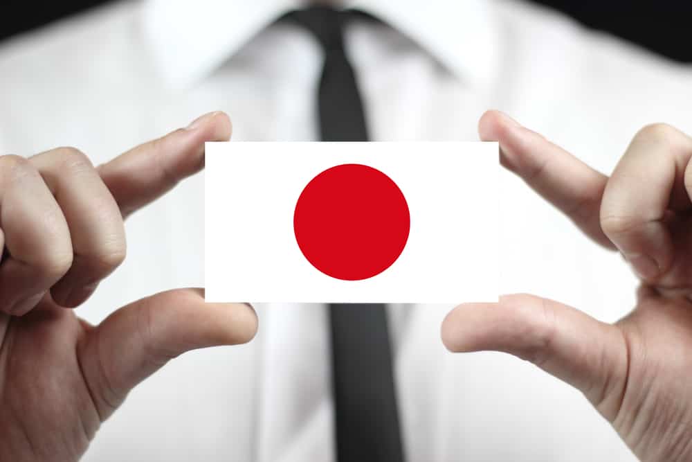 The fingers of someone is holding up an illustration of the Japanese flag. The person's body is blurred in the background.