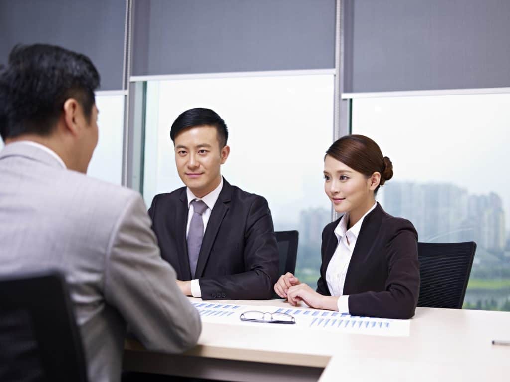 Young Asian man and woman talking to another man, who seems like their superior in an office.