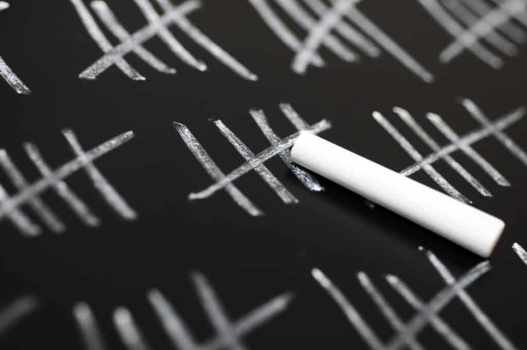 A photo of a black board with tally marks all over it. The tally marks are in bundles of 5, with a piece of white chalk in the center of the blackboard.
