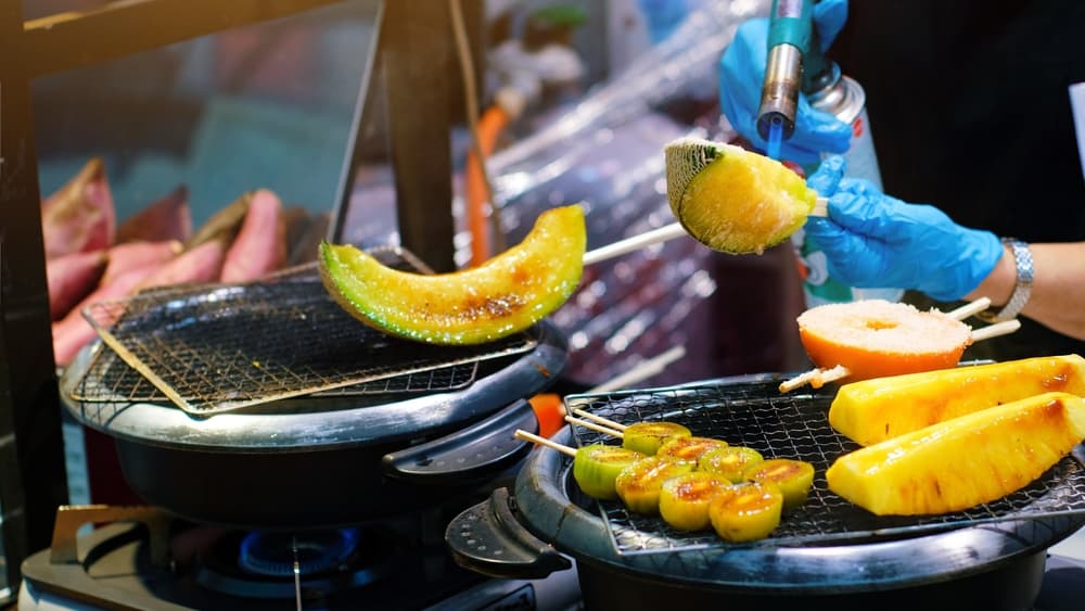 Food vendor at the outdoor Kuromon Market in Osaka. They are grilling slices of melon with a blowtorch.