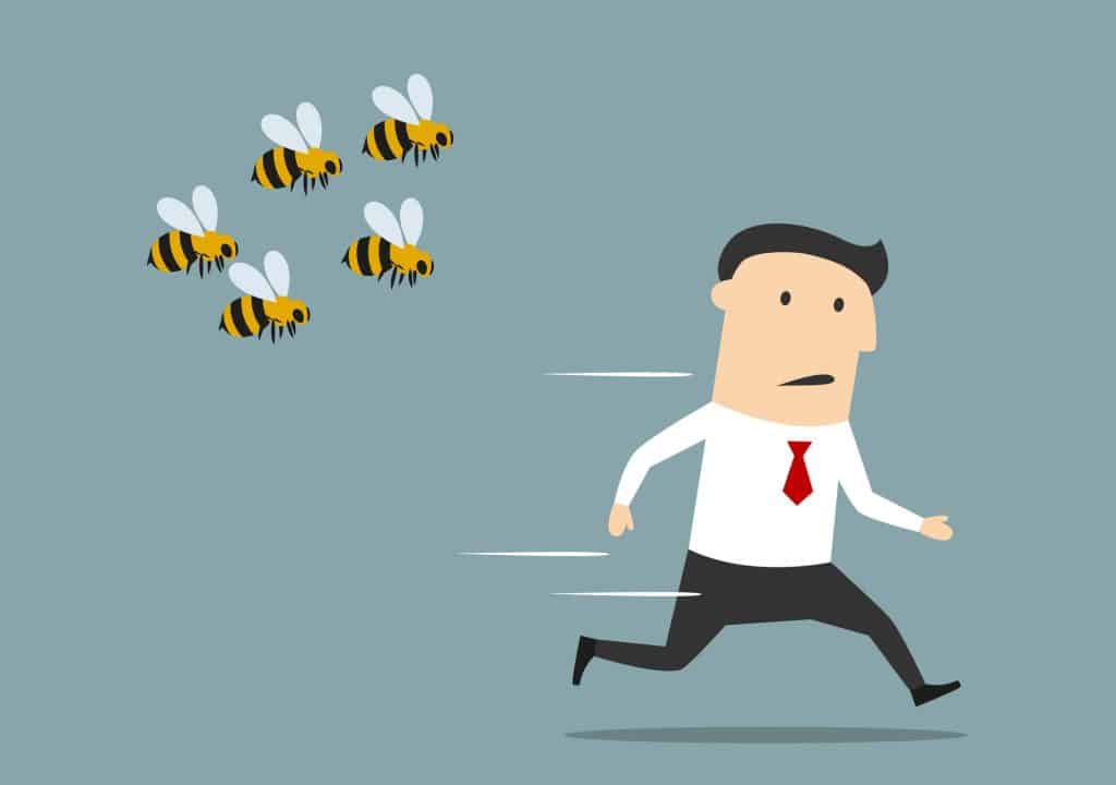 A cartoon illustration of a businessman was attacked by swarm of angry bees (to the left of the image). The man is wearing a long sleeve white shirt, black pant trousers, and a red tie.
