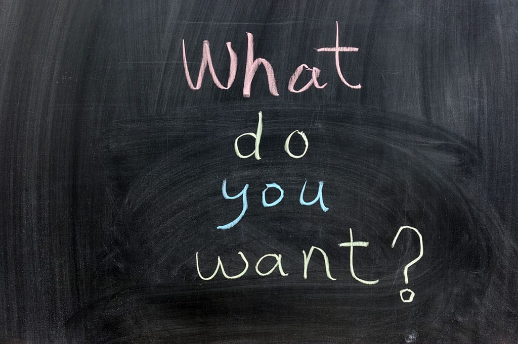 A blackboard with the text, "What do you want?" written on it in different colors (pink, yellow, blue, yellow).
