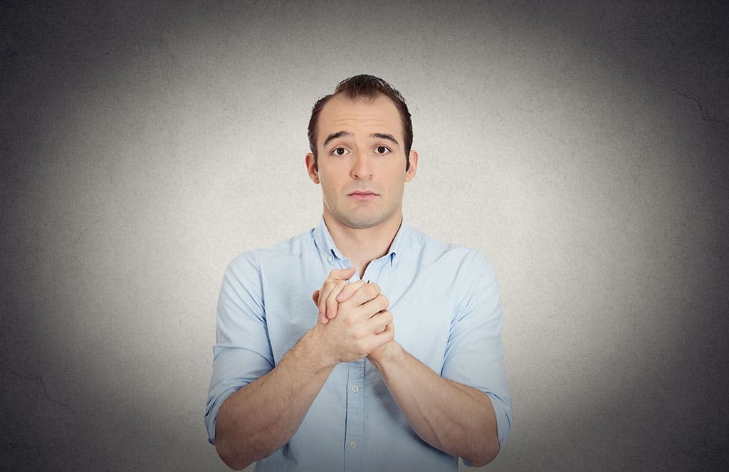A middle aged man clasping his hands together with his facial expression looking as if he is asking for a favor.