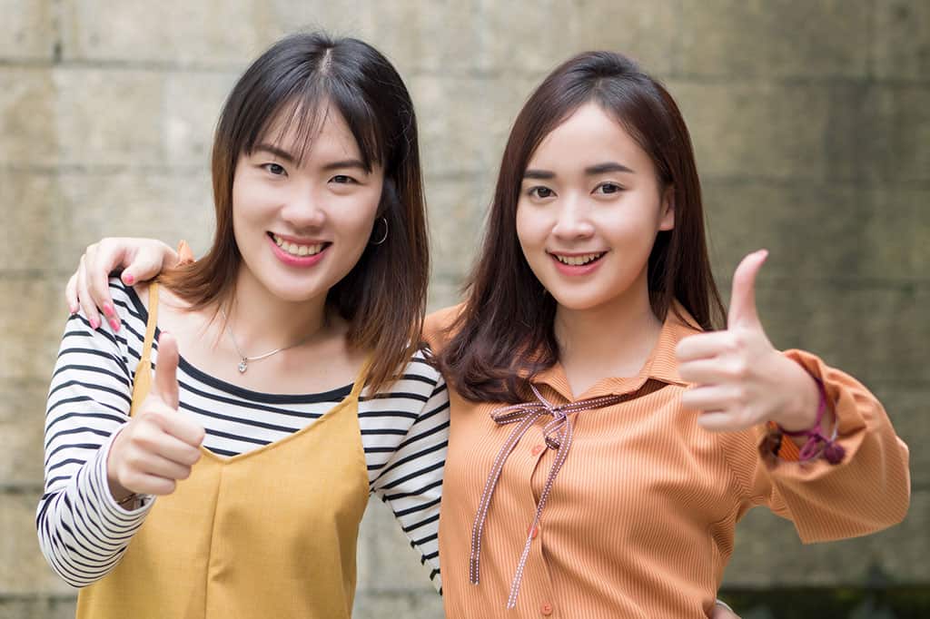 Two young women giving the "thumbs up" sign with their hands and smiling.  