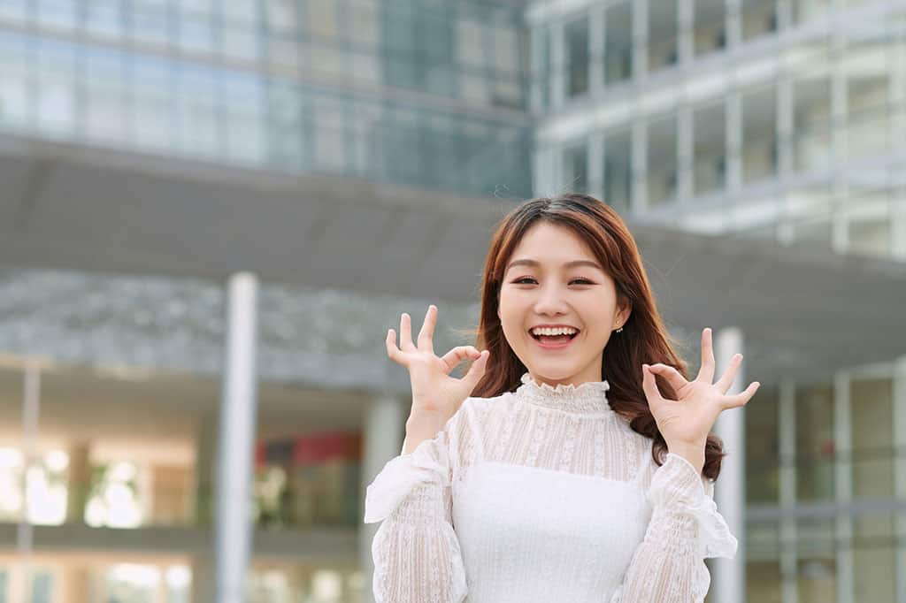 A young woman doing the "OK" gesture with both of her hands while smiling.