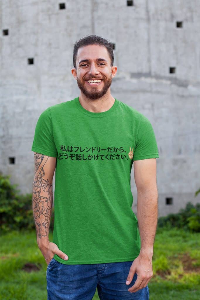 A young man with a beard wearing a green shirt with Japanese text on it, as well as an illustration of a peace sign formed by a small hand. The Japanese text translates to "I'm friendly, so please come talk to me."