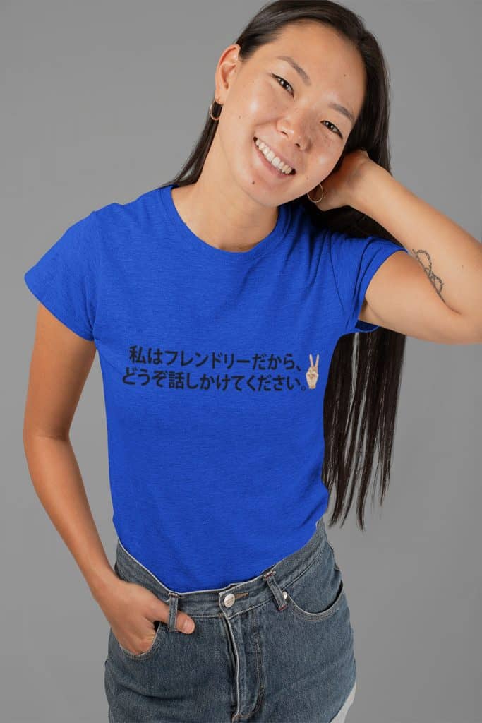 A young Asian woman wearing a blue shirt with Japanese text and an illustration of a hand showing a peace sign. The Japanese text translates to "I'm friendly, so please come talk to me."