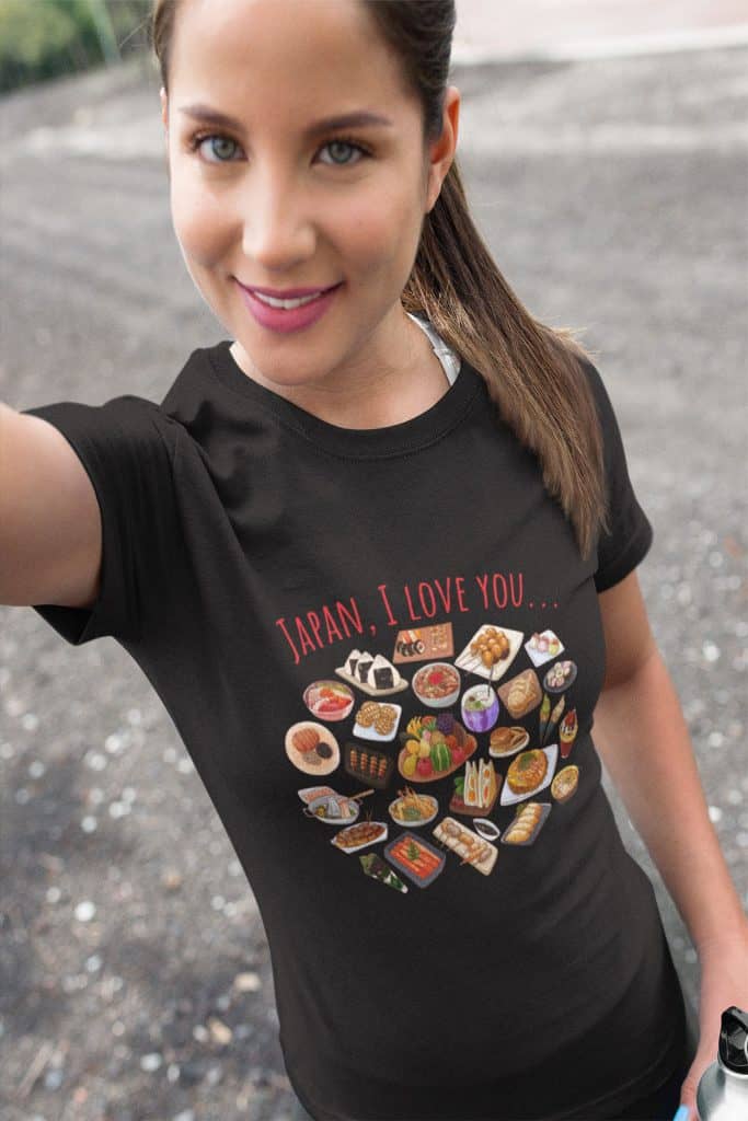 A young woman taking a selfie from above. She is wearing a black shirt that reads, "Japan, I Love You." on it. There are many illustrations of foods from Japan on the shirt.