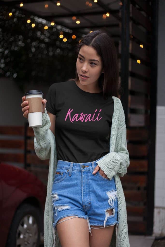 A young girl holding a paper coffee cup wearing a black shirt that says "Kawaii" on it in cursive font.