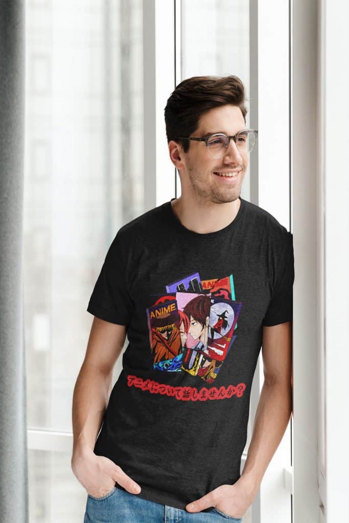 A young man with glasses learning against a wall, wearing a black shirt that has illustrations of anime titles on it. The shirt has Japanese text written on it that translates to, "Shall we talk about anime?"