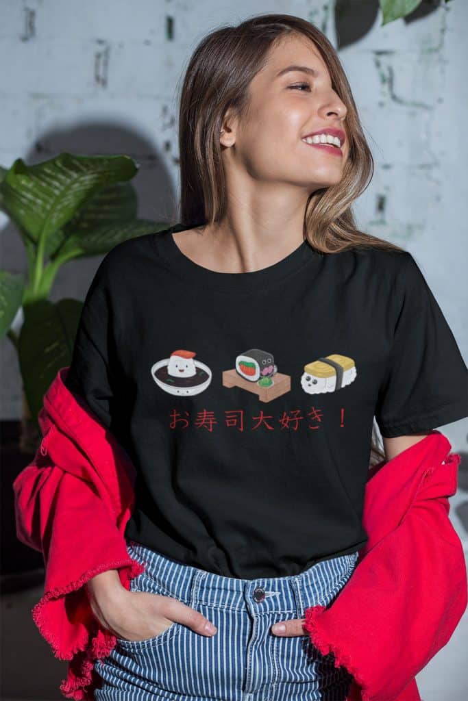 A young girl wearing a black shirt with green leaf plants in the background. The Japanese text on the black shirt reads translates to, "I love sushi!" There are 3 cute sushi characters on the shirt.