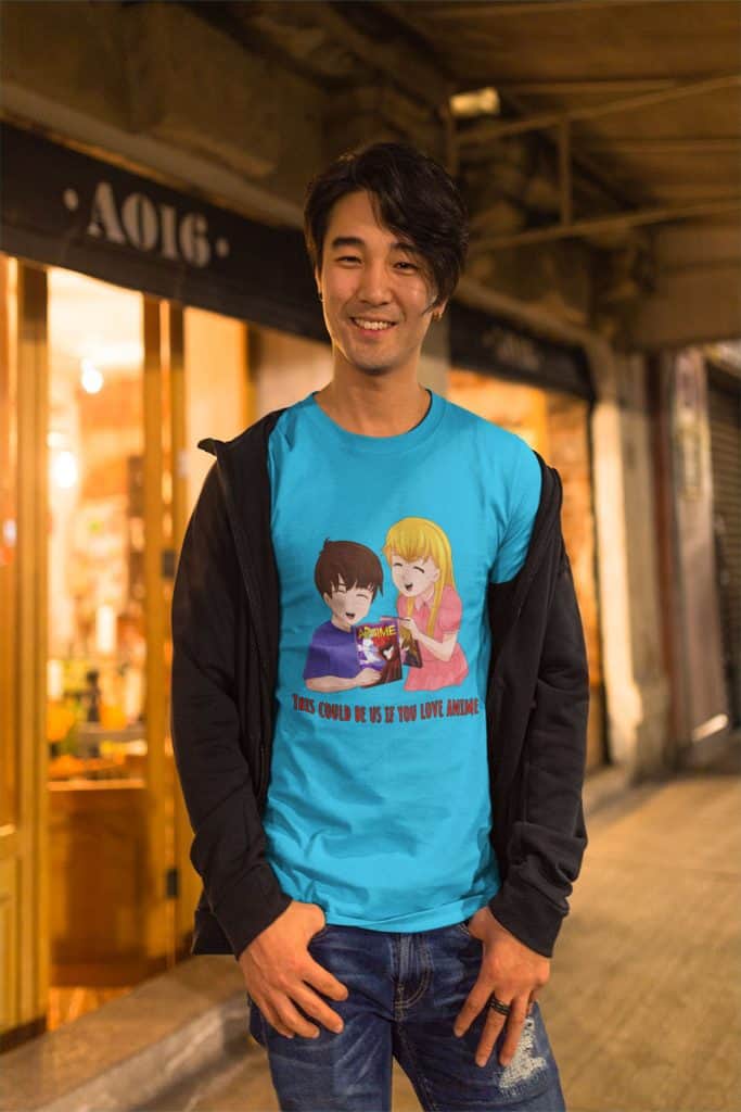 A young Asian man standing in front of a store wearing a blue shirt with a boy and girl illustration on it, looking at anime titles. The text on it reads, "This could be us if you love anime."