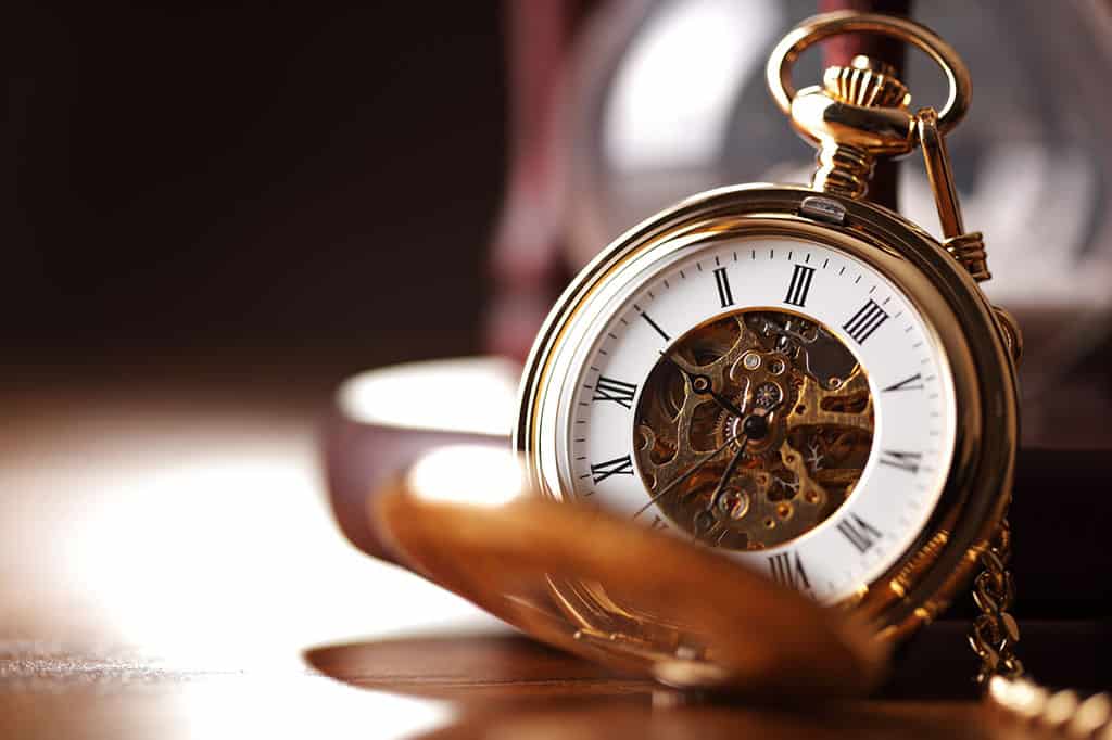 A gold, open pocket watch with its face visible is resting on a tabletop with the background blurred.