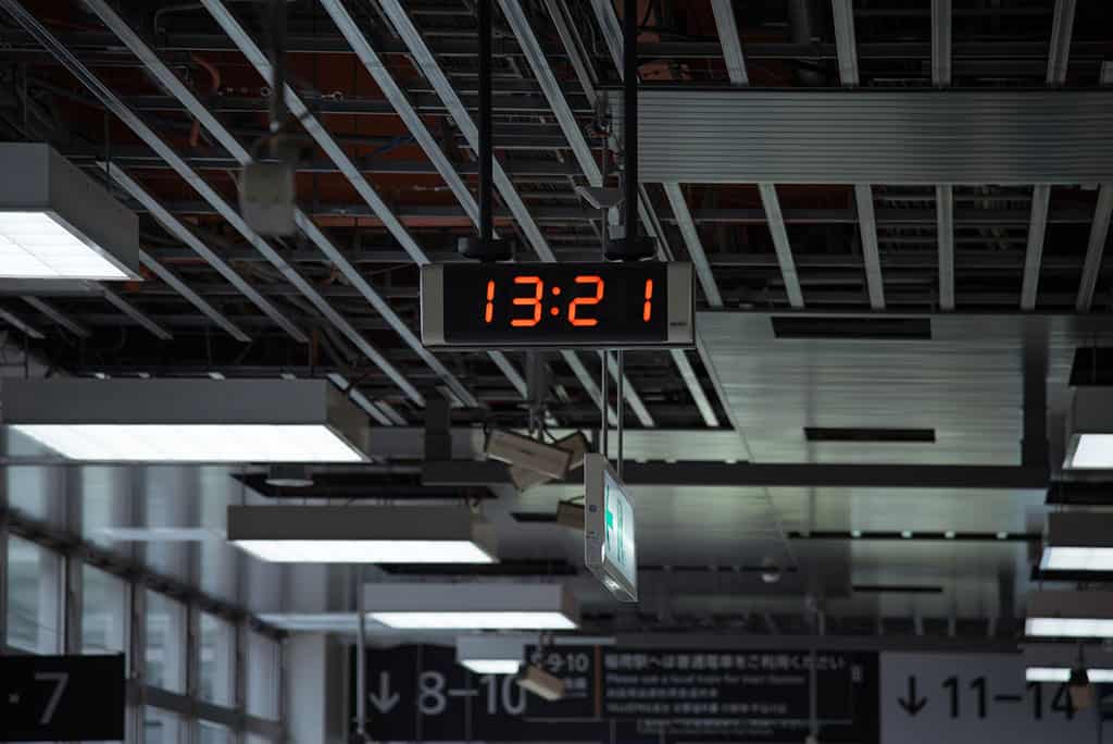 A digital clock at a train station that is displaying the time, "13:21."