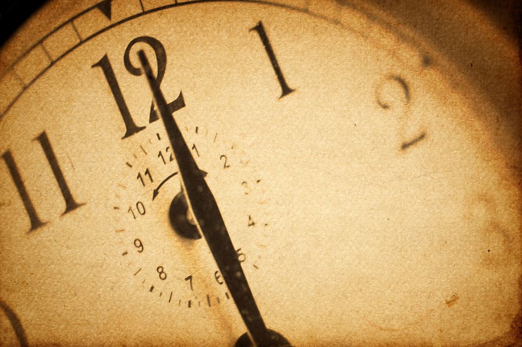 A close up or a clock that has one of its hands (the only visible one) pointing to 12.