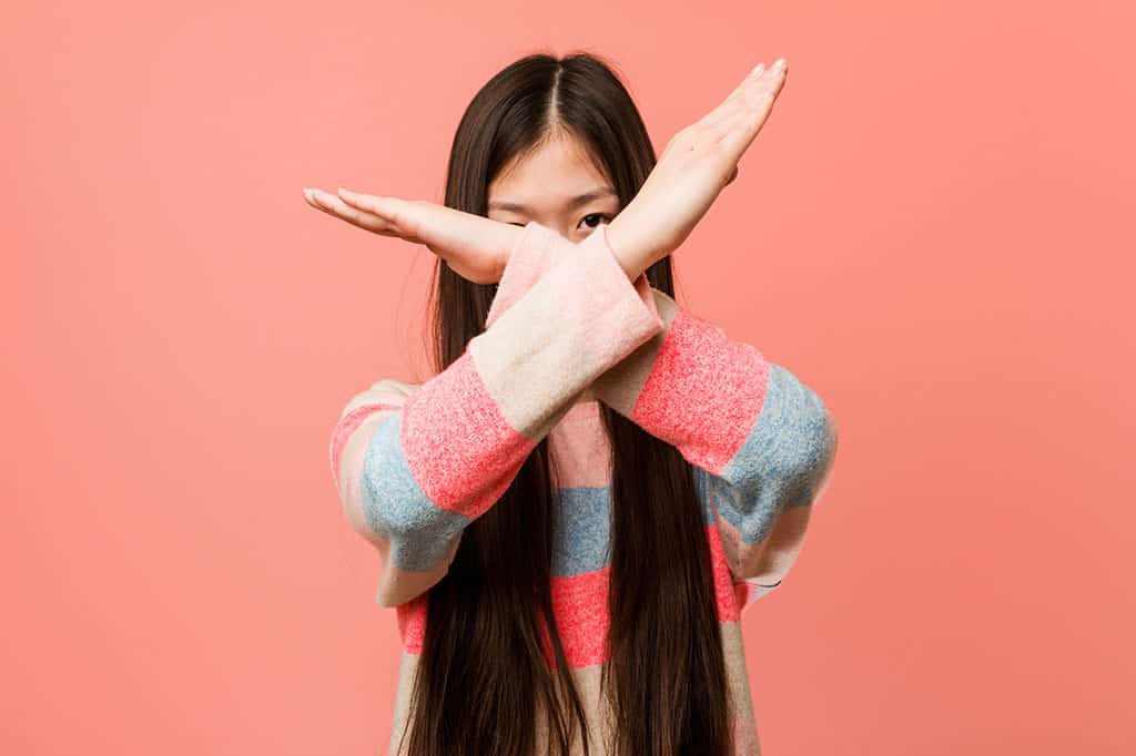 A young, Asian woman crossing her arms in front of her face to form an "X."