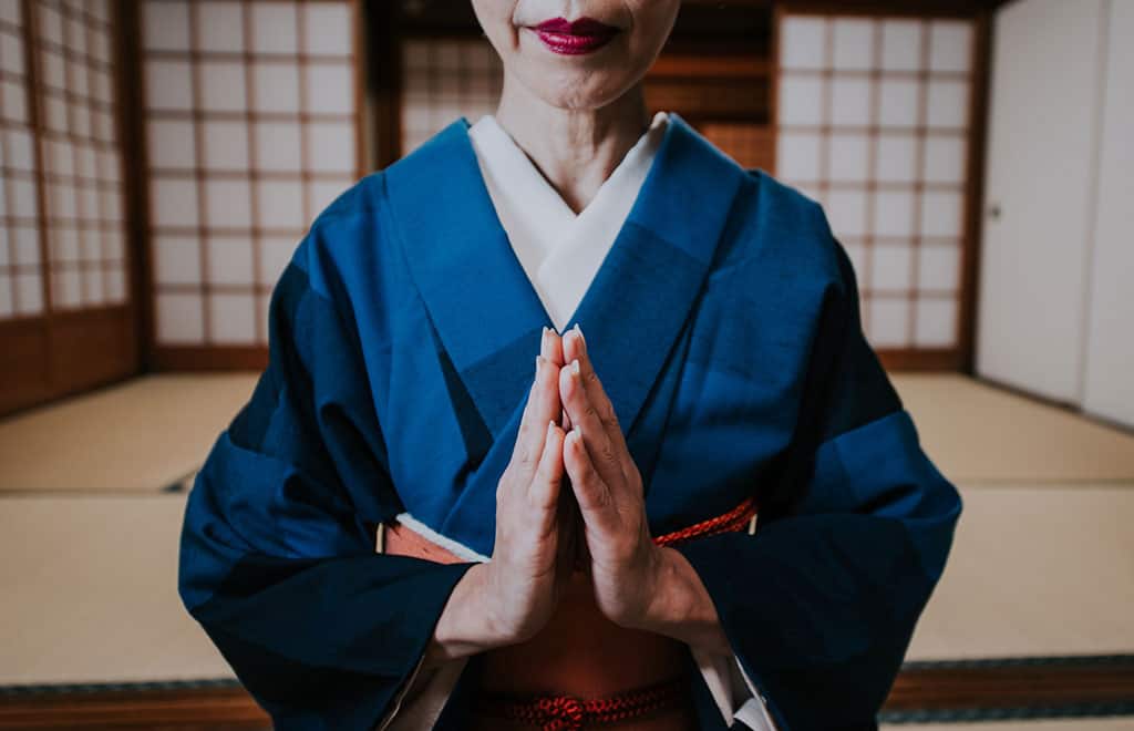 A woman dressed in traditional Japanese clothes with her hands together as if in prayer or saying please.