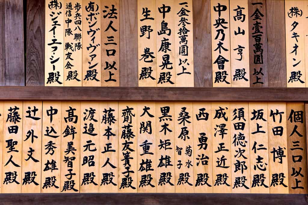 Many wooden signs, each with Japanese characters on it. The signs on on a wall of some sort.