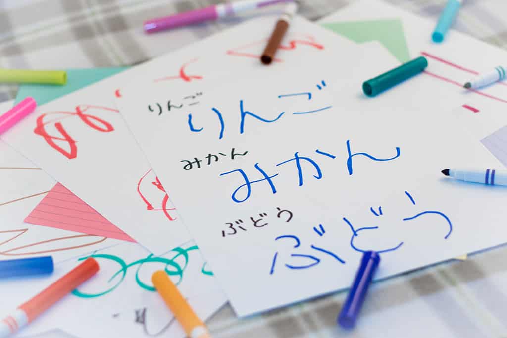 Japanese words written in hiragana on a small sheet of paper. Colored pens and other stationary can be seen.