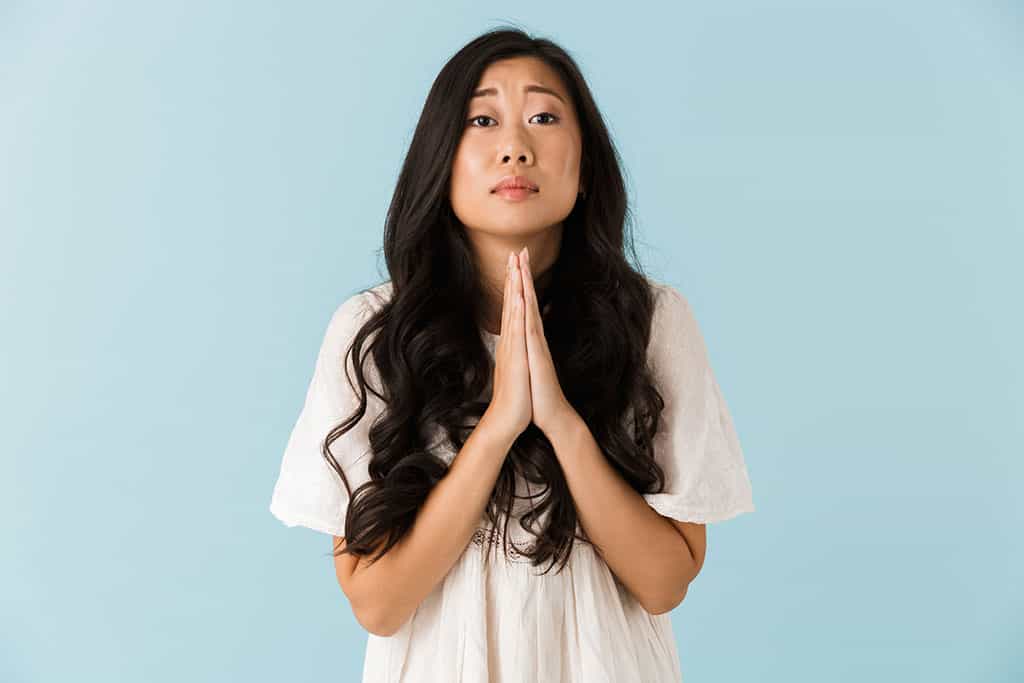 A young Asian woman who has her hands together to ask for something.