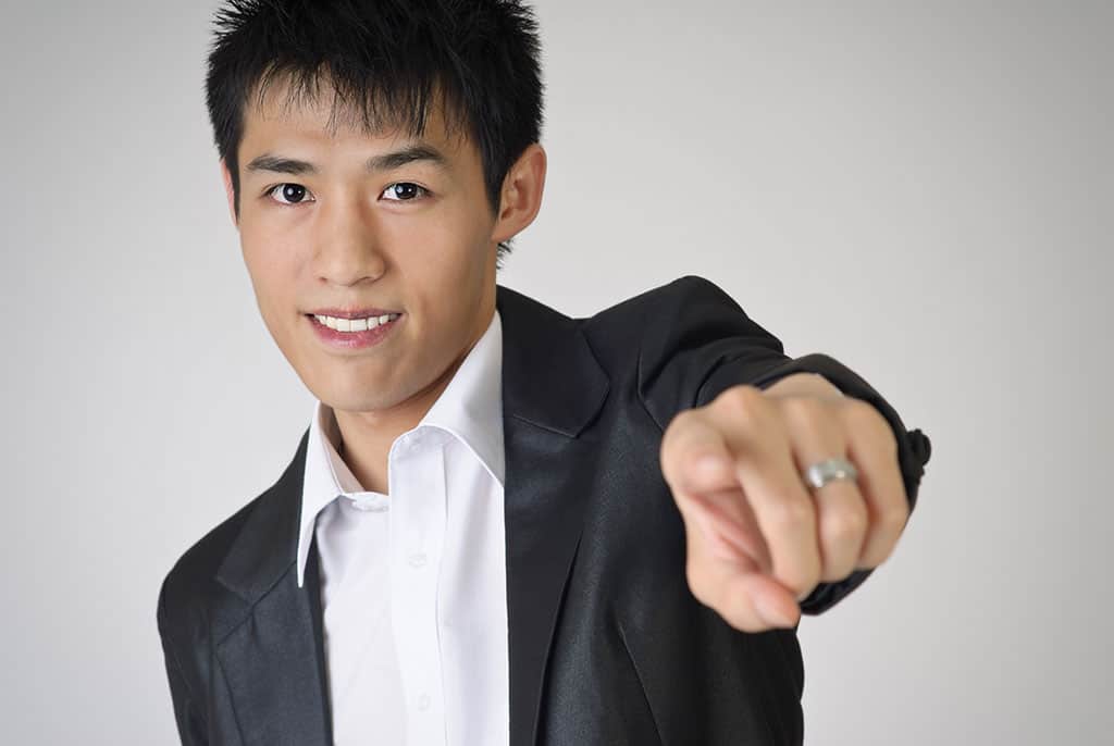 An Asian man in a suit pointing at the camera and smiling