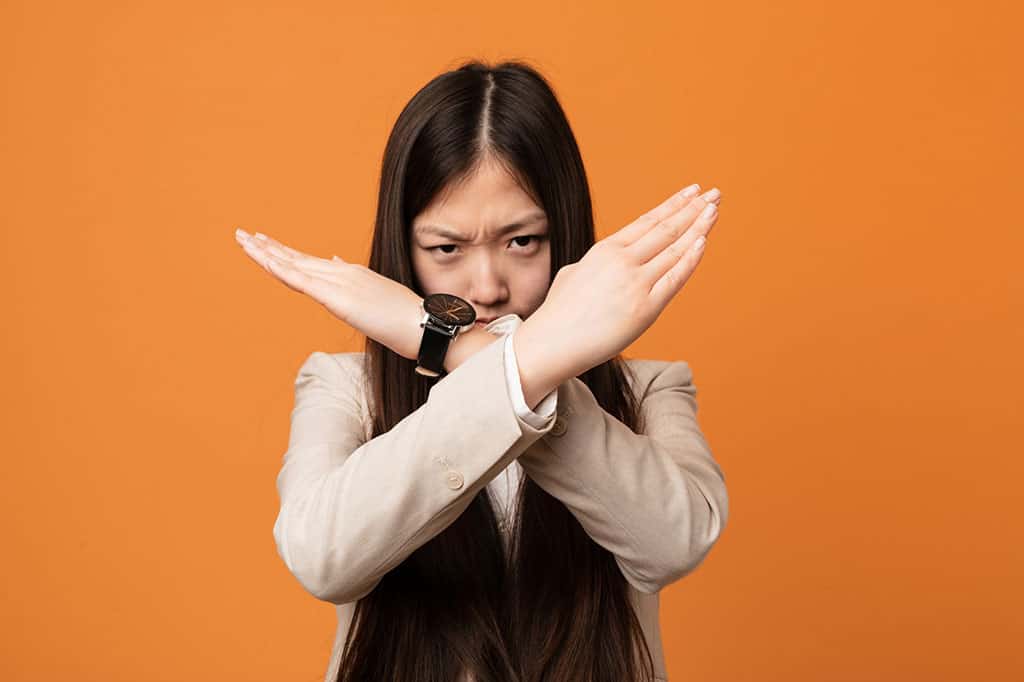 A young, Asian woman with her arms crossed in front of her face to form an "X" shape.