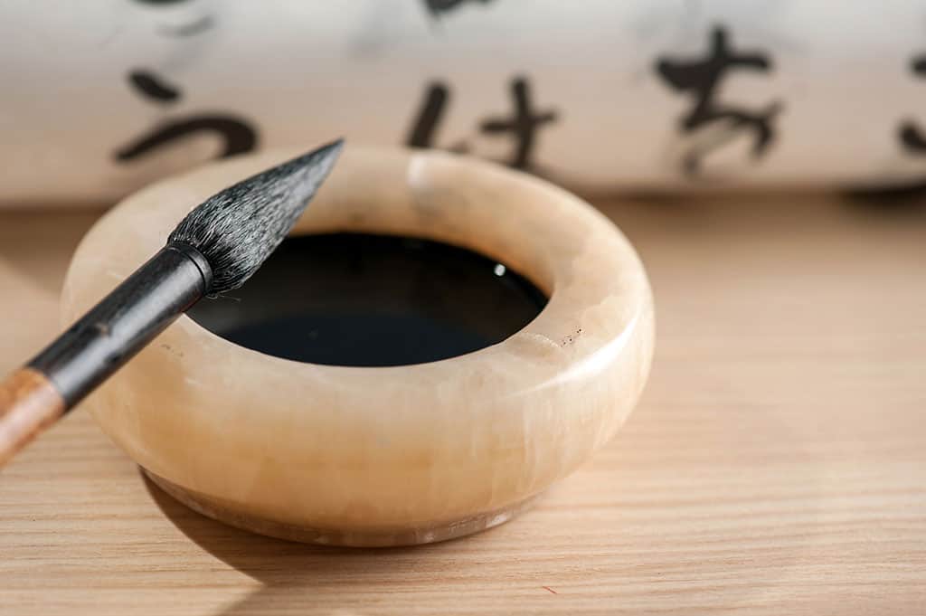 A calligraphy brush resting on a nice bowl filled with black ink.