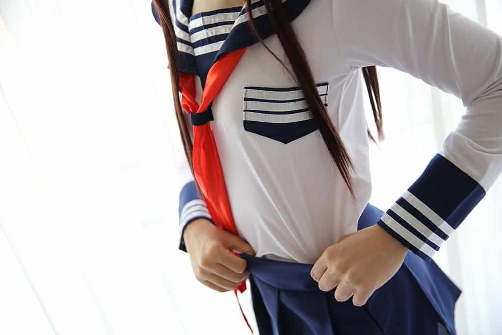 A girl putting on a Japanese school uniform (a white shirt with blue skirt and red tie).