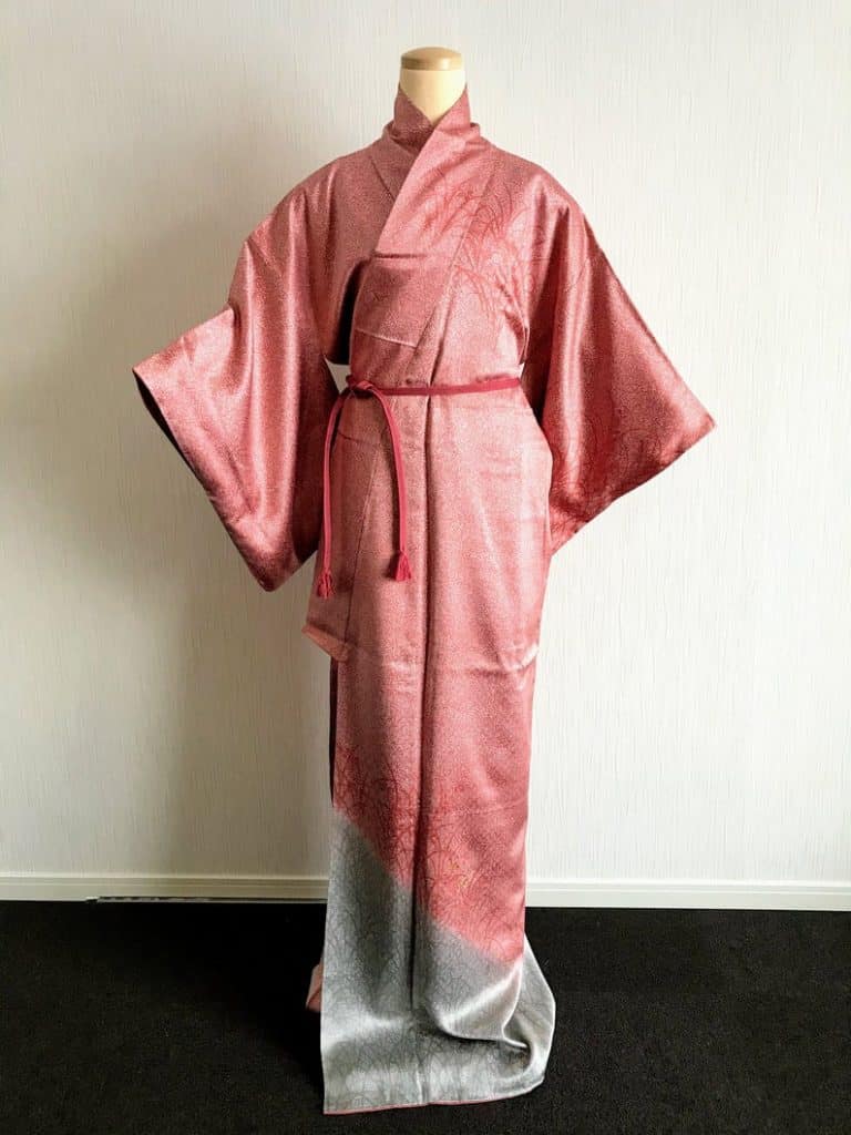 A full-body, pink kimono with silver trimmings at the bottom displayed on a mannequin.  