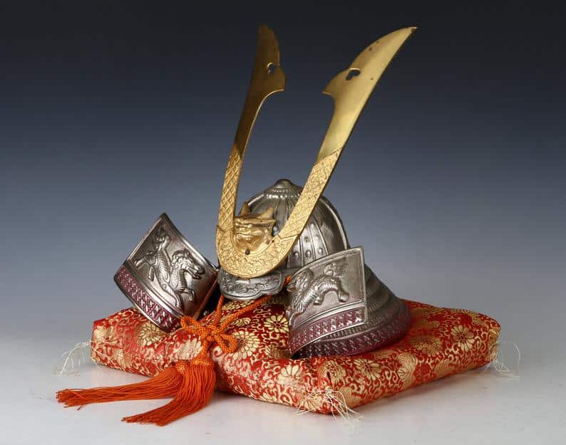 A metal Japanese samurai looking helmet resting on a red and gold cushion.