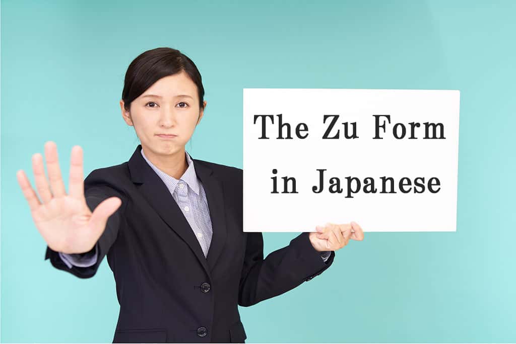 A younger, Asian woman in a black business suit with her right hand out as if to say, "stop." She is holding a white board that reads, "The Zu Form in Japanese."