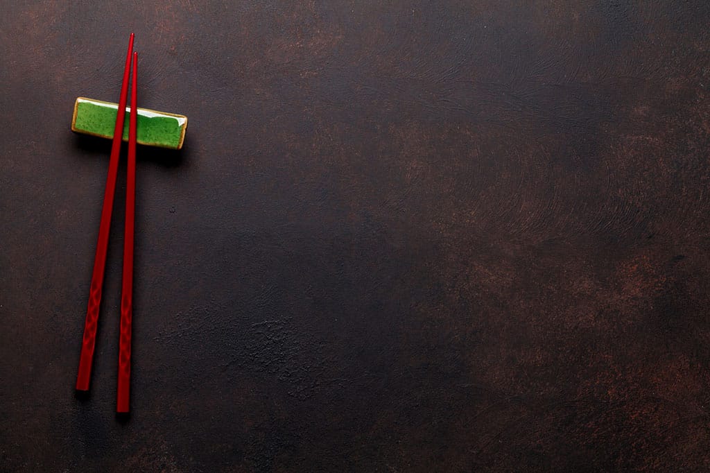 A pair of red chopsticks on a green chopstick rest. Both are on a brown blackish table.