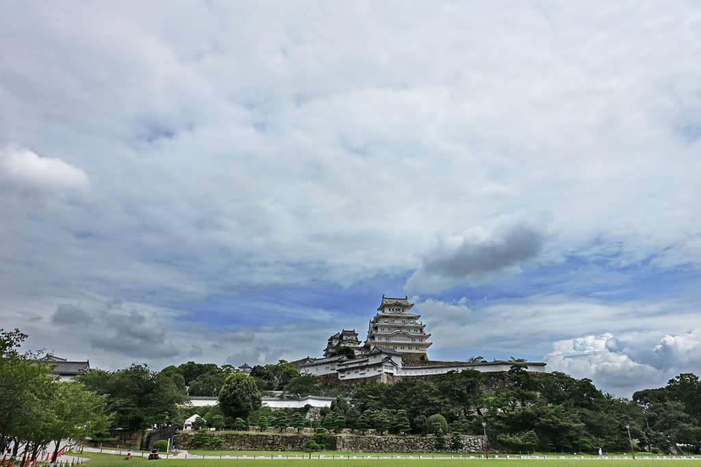 The Himeji Castle seen from afar, with the surrounding landscape and sky visible all around. There is text in it that reads, "The Sou Form in Japanese: It Looks Like ~ I Hear That ~"