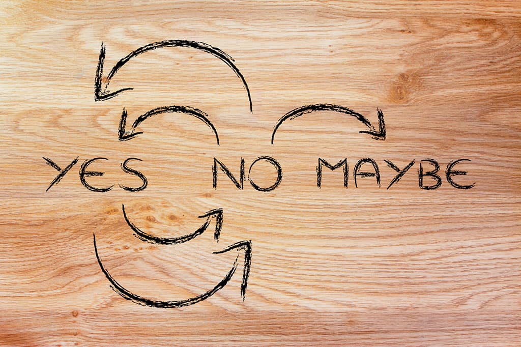 A wooden background with the words "YES NO MAYBE" written on it with arrows flowing and connecting the words to one another.