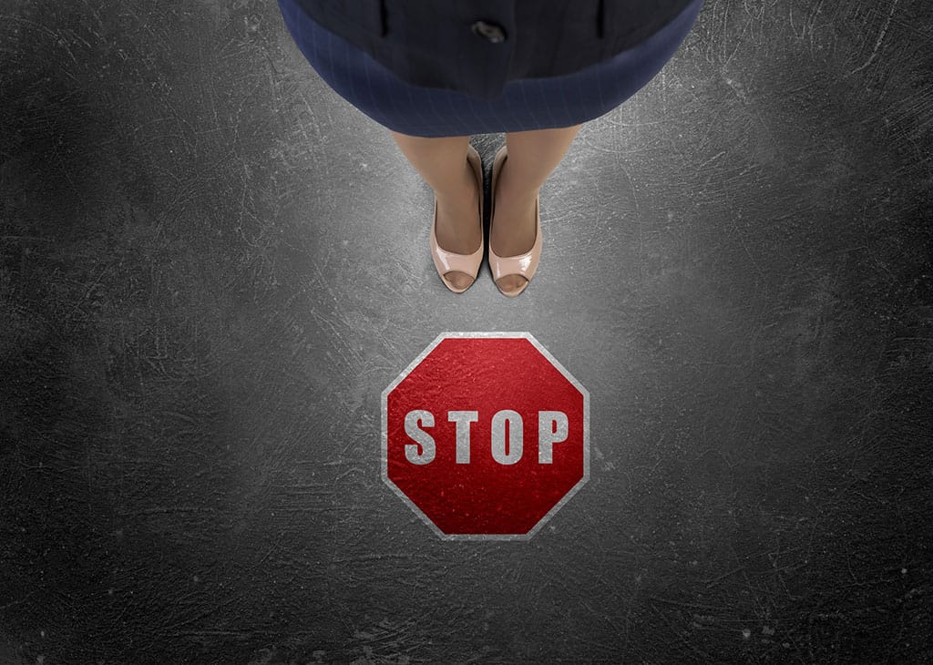 A red stop sign printed on the floor with a woman's legs visible standing behind it.