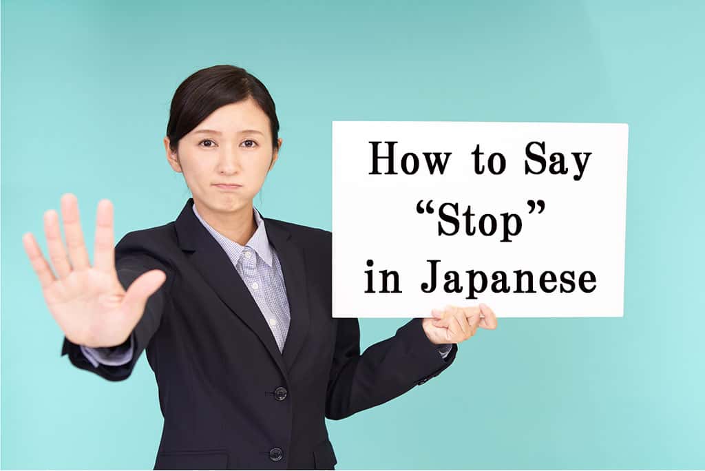 An Asian woman in a black business jacket and blue checkered shirt holding out her right hand as if to say "stop." Her left hand is holding a white sight that has the text, "How to Say "Stop" in Japanese" on it.