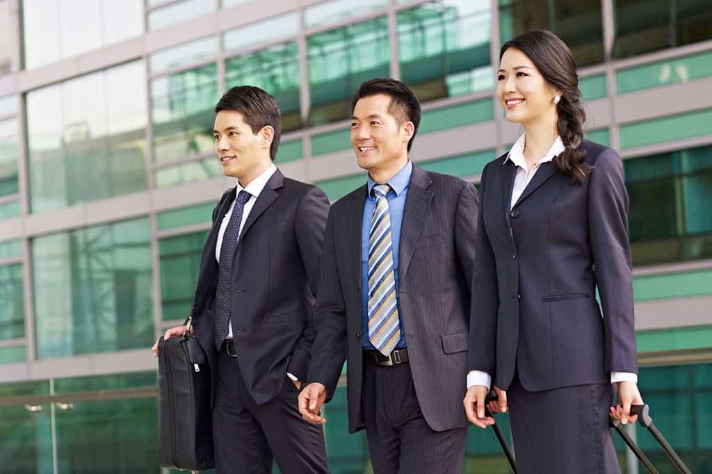 Two Asian men and a young, Asian woman dressed in business suits, all standing next to each other and smiling.