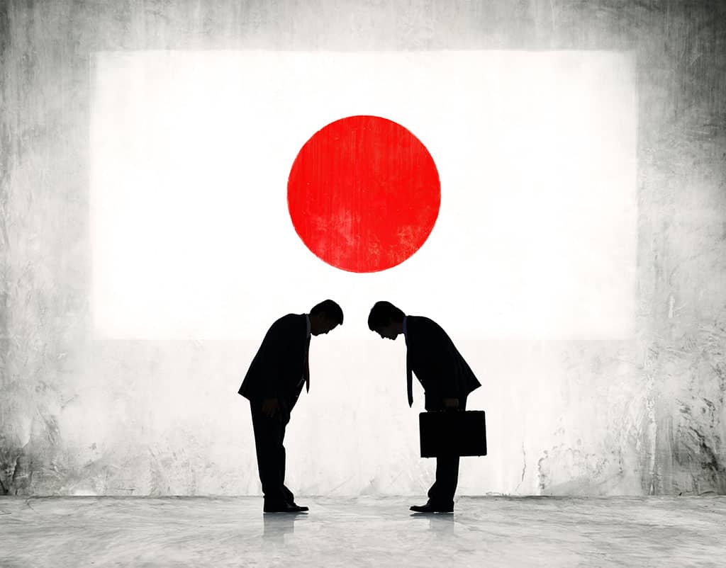 An illustration of two silhouettes of men facing each other and bowing. The man on the right is holding a briefcase. There is a big flag of Japan in the background.